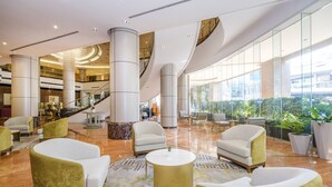 Een ruime lobby met hoge plafonds, een centrale trap en een zithoek met moderne fauteuils en een salontafel.