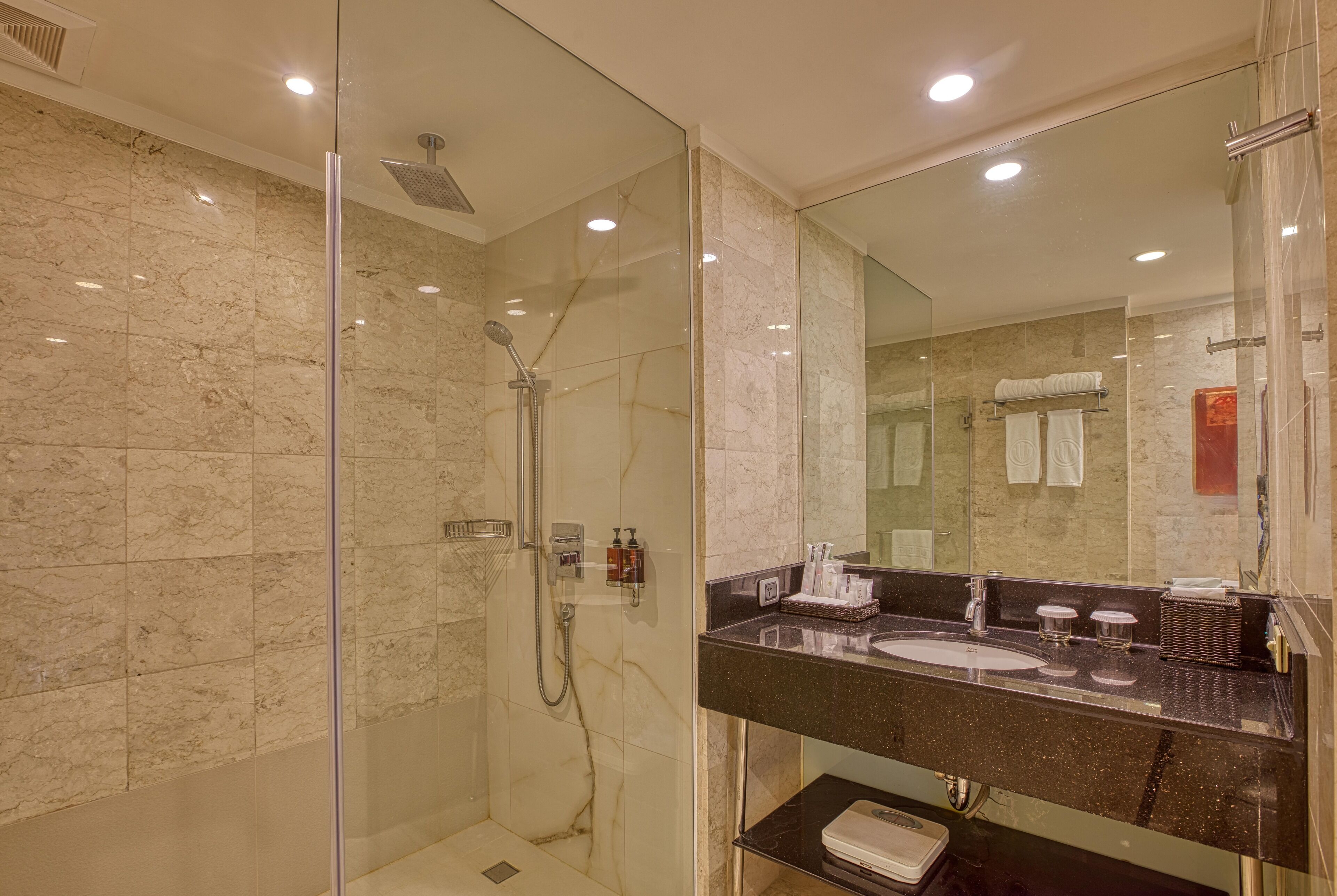 A modern bathroom with a glass-enclosed shower, a black marble sink, and a large mirror.