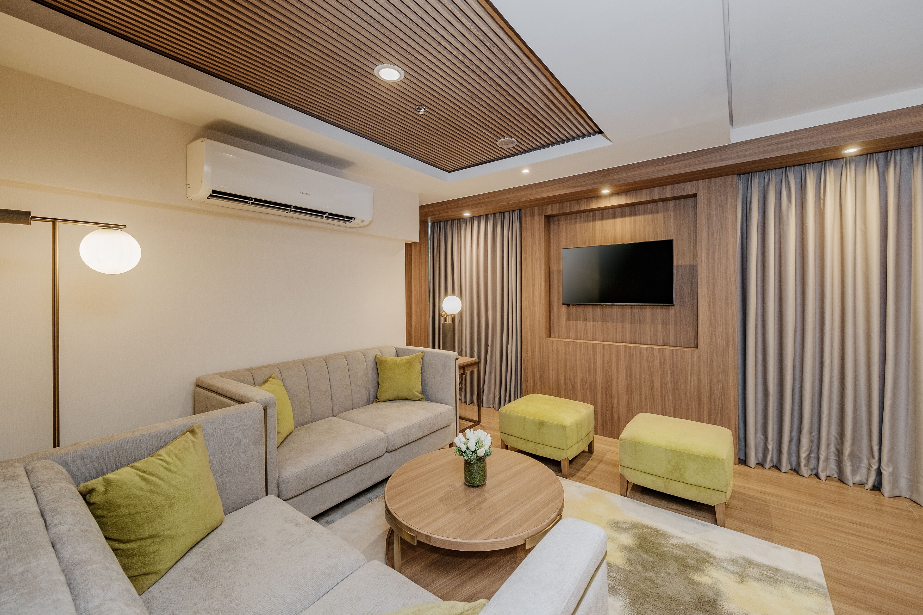 A modern living room with a sofa, ottoman, coffee table, and a flat-screen TV mounted on the wall.
