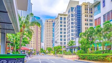 A city street with a bus stop sign, tall buildings, and palm trees.