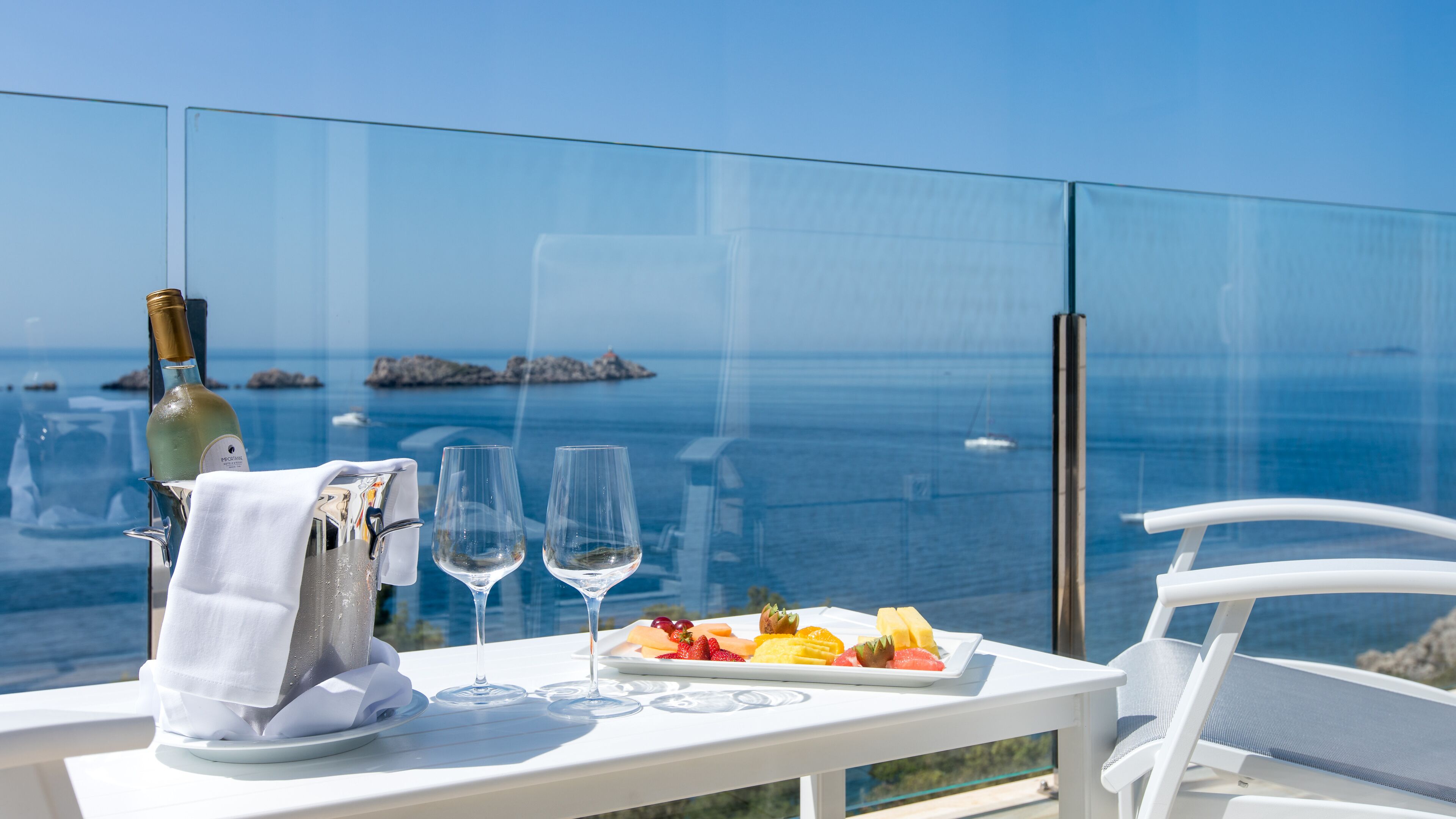 A table with a bottle of white wine, two glasses, and a plate of fruit.