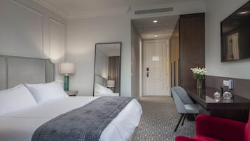 A hotel room with a large bed, a desk, a chair, and a mirror.