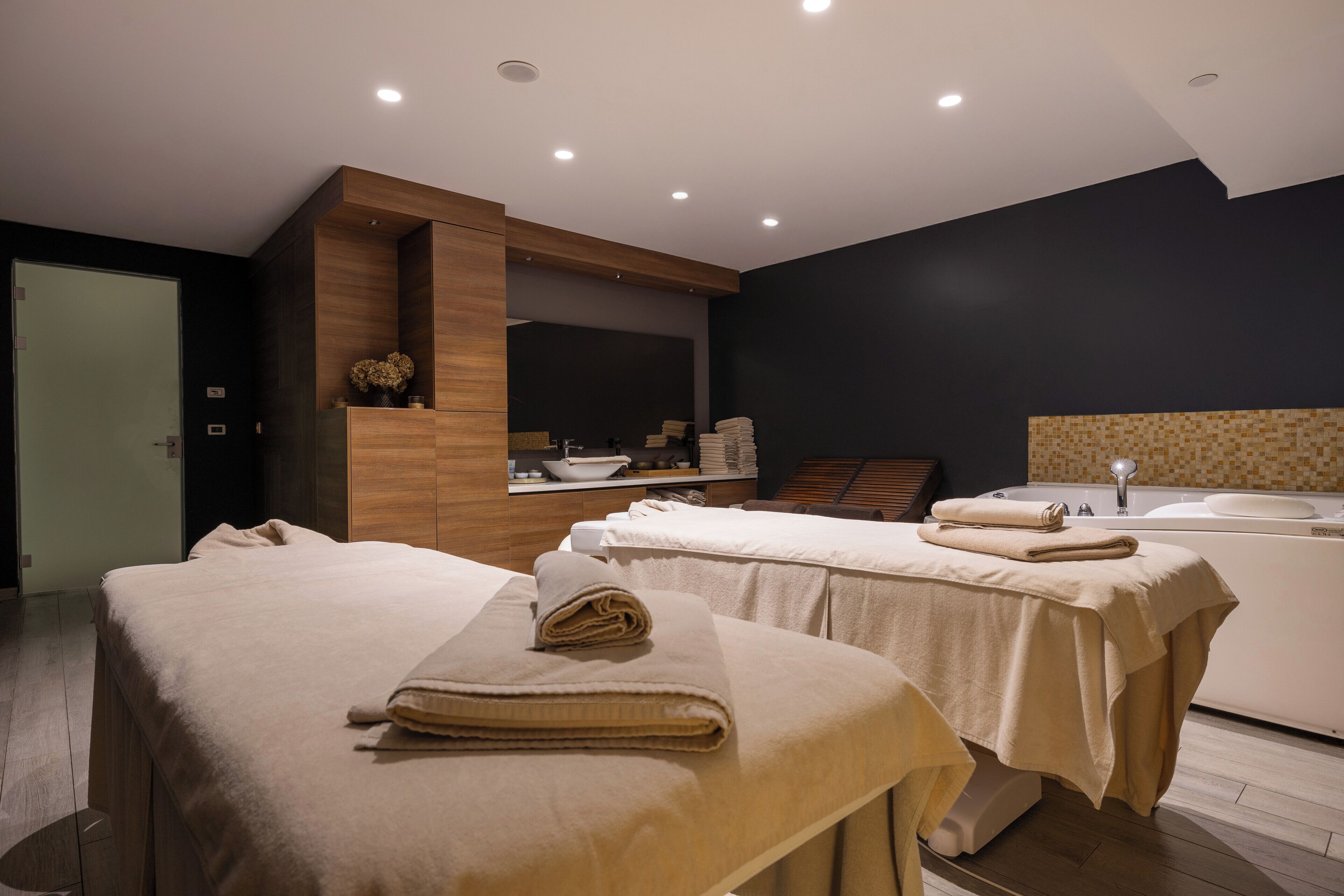Una moderna sala spa con due lettini per trattamenti, una grande vasca da bagno e un'accoglienza in legno.
