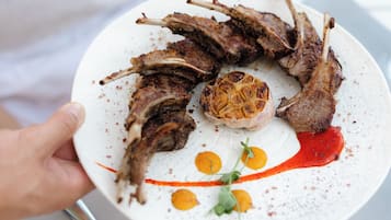 A plate with grilled lamb chops, a roasted garlic centerpiece, and a decorative sauce.