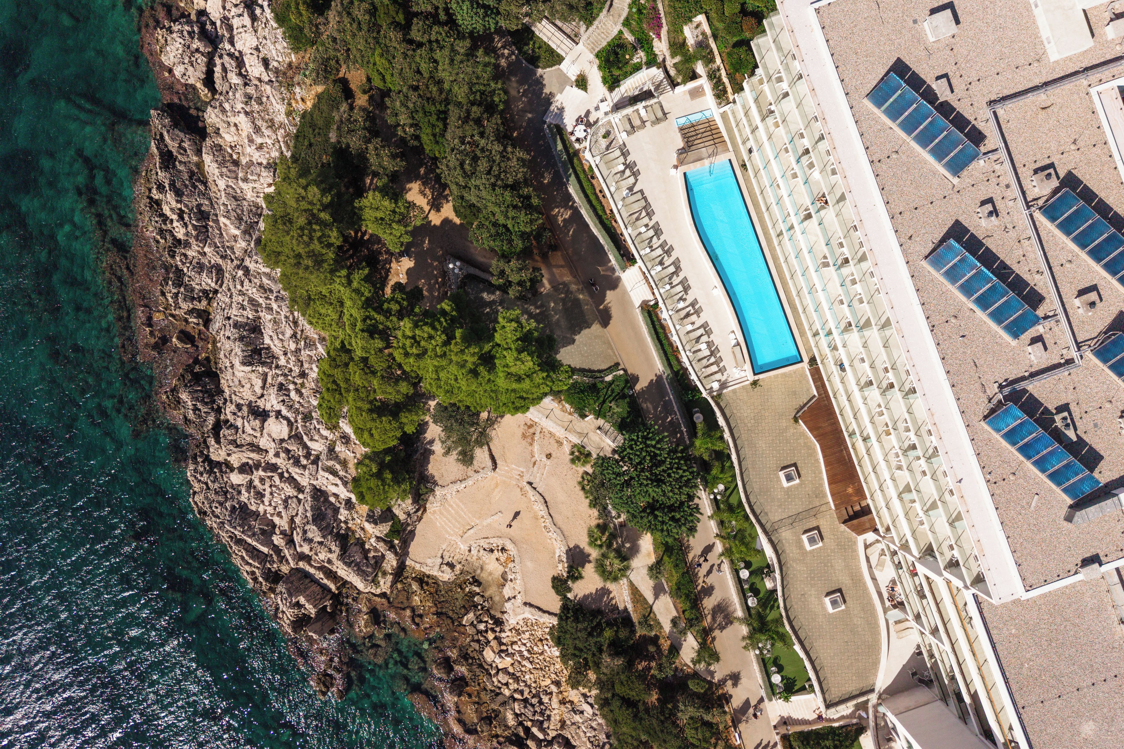 An aerial view of a coastal property with a swimming pool, rocky terrain, and a building with multiple balconies.