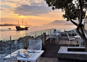 A seaside restaurant with outdoor seating overlooking the sea, a ship in the background, and a clear sky. - Royal Palm Hotel (Dubrovnik)