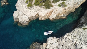 Vue aérienne d’une zone côtière avec des eaux turquoise limpides, des falaises rocheuses et un bateau ancré près du rivage.