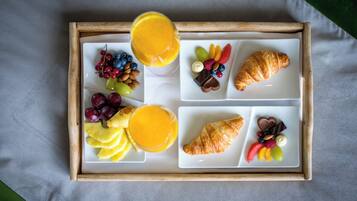 Bandeja de café da manhã com croissants, frutas e suco de laranja.