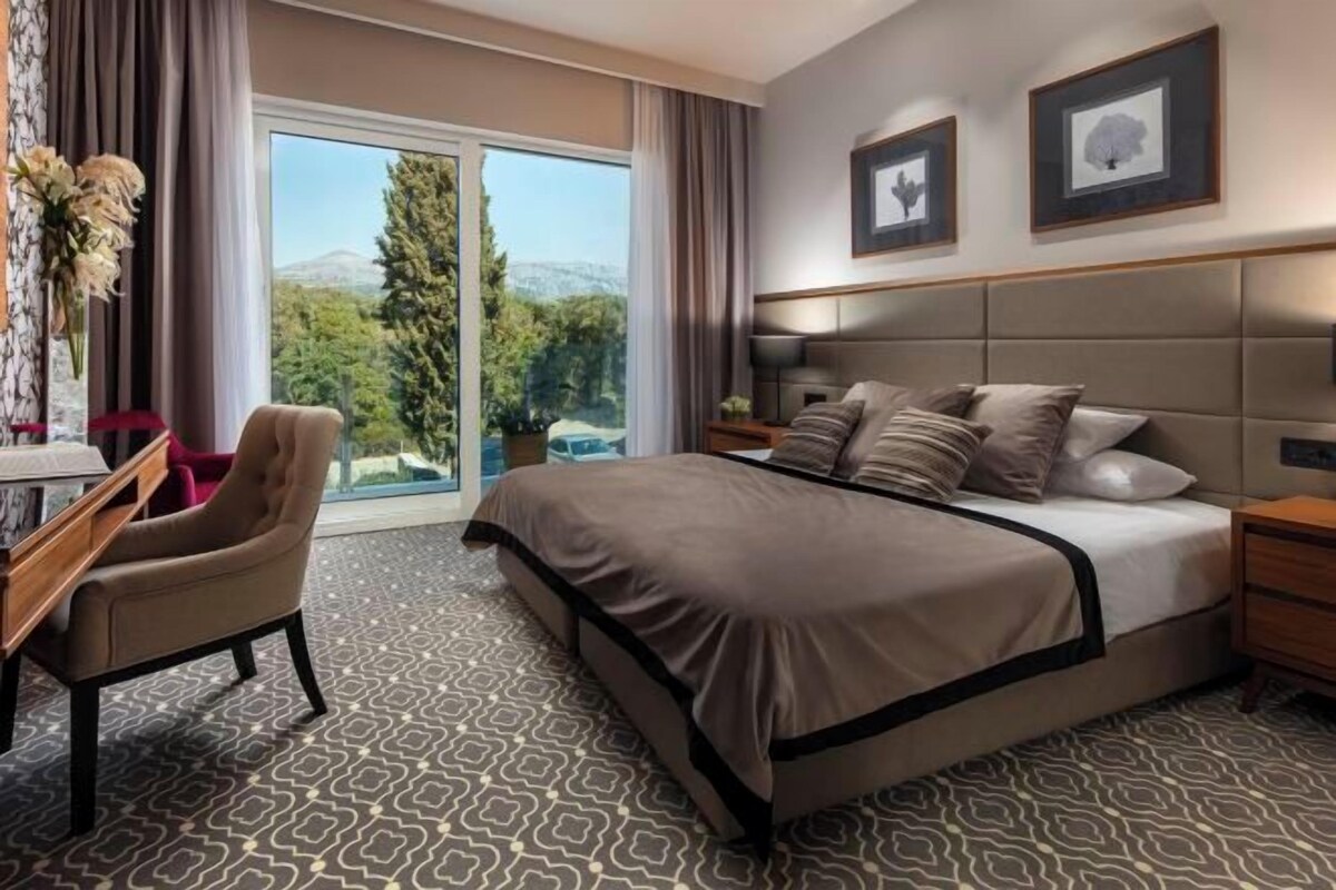 Habitación de hotel con una cama grande, un escritorio, una silla, una mesita de noche y vistas al exterior.