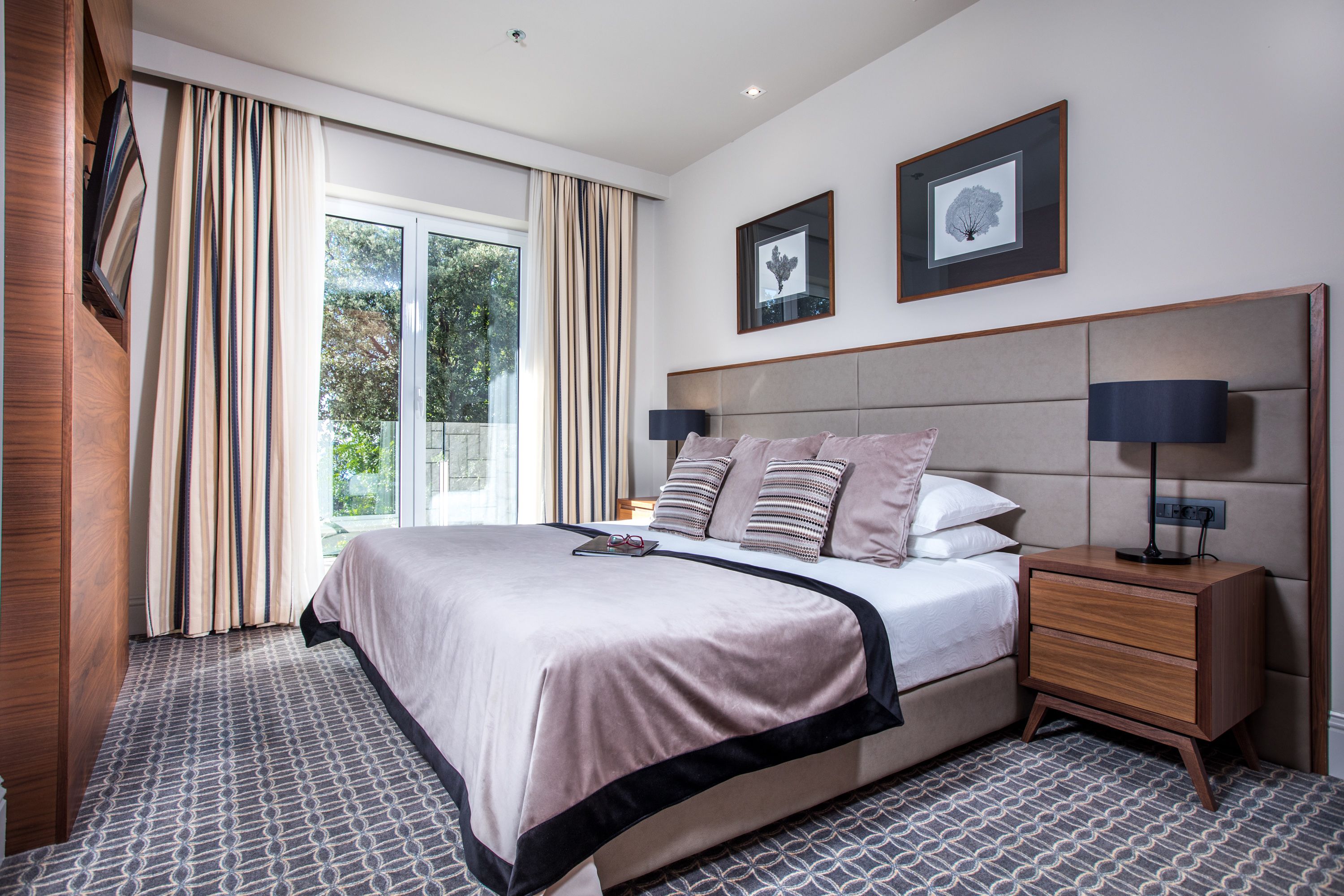 A modern hotel room with a large bed, a nightstand, and a window with curtains.