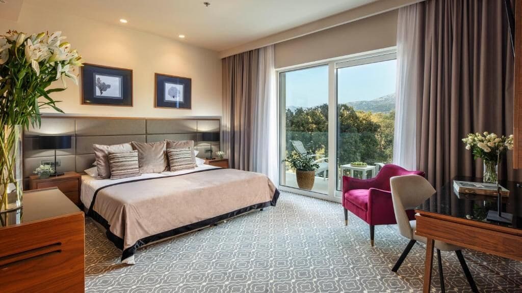 Una habitación de hotel moderna con una cama grande, un escritorio y una silla. Cuenta con un balcón con vistas al exterior.