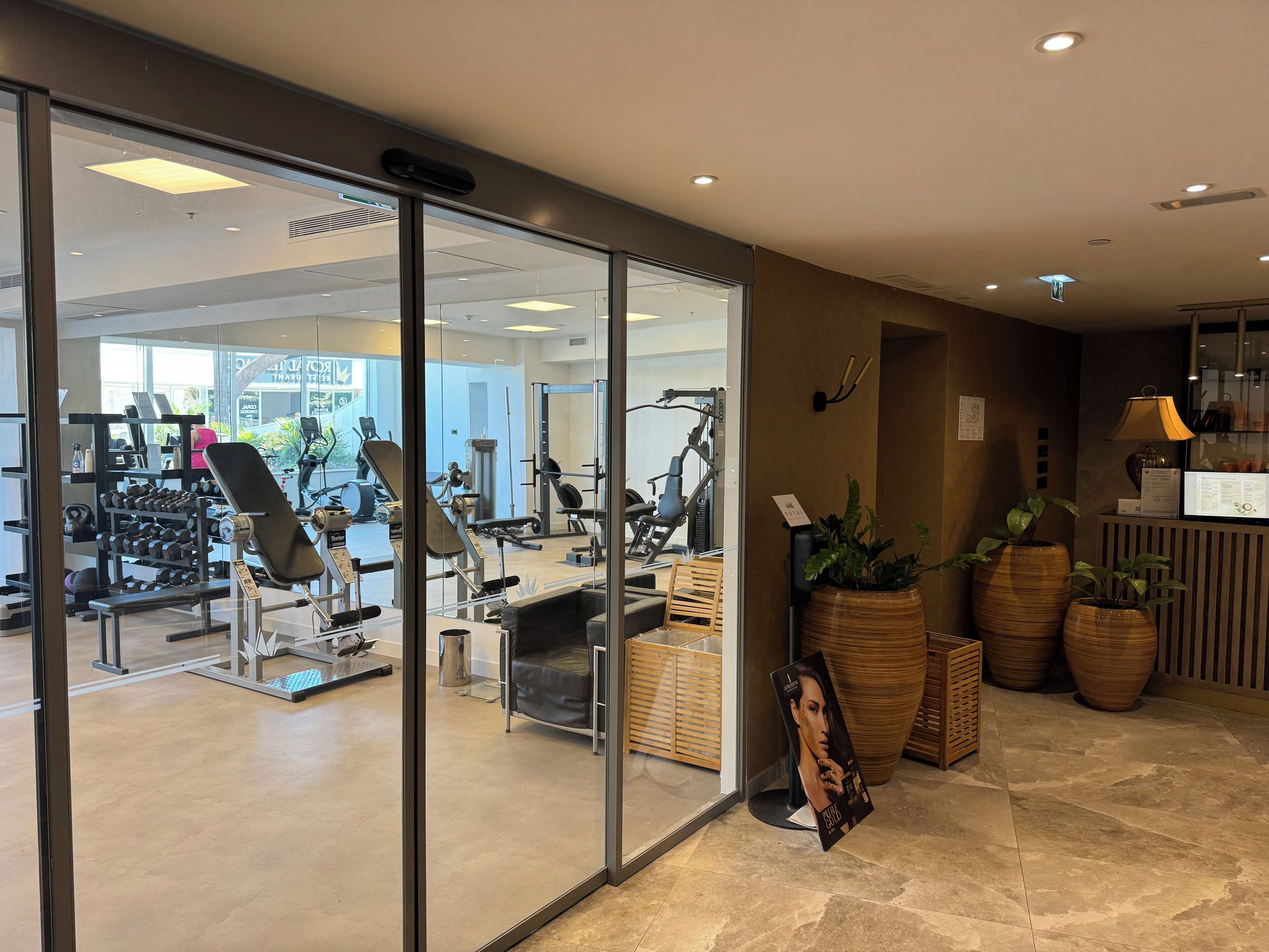 Un gimnasio moderno con paredes de vidrio, equipo de ejercicio y plantas en macetas.