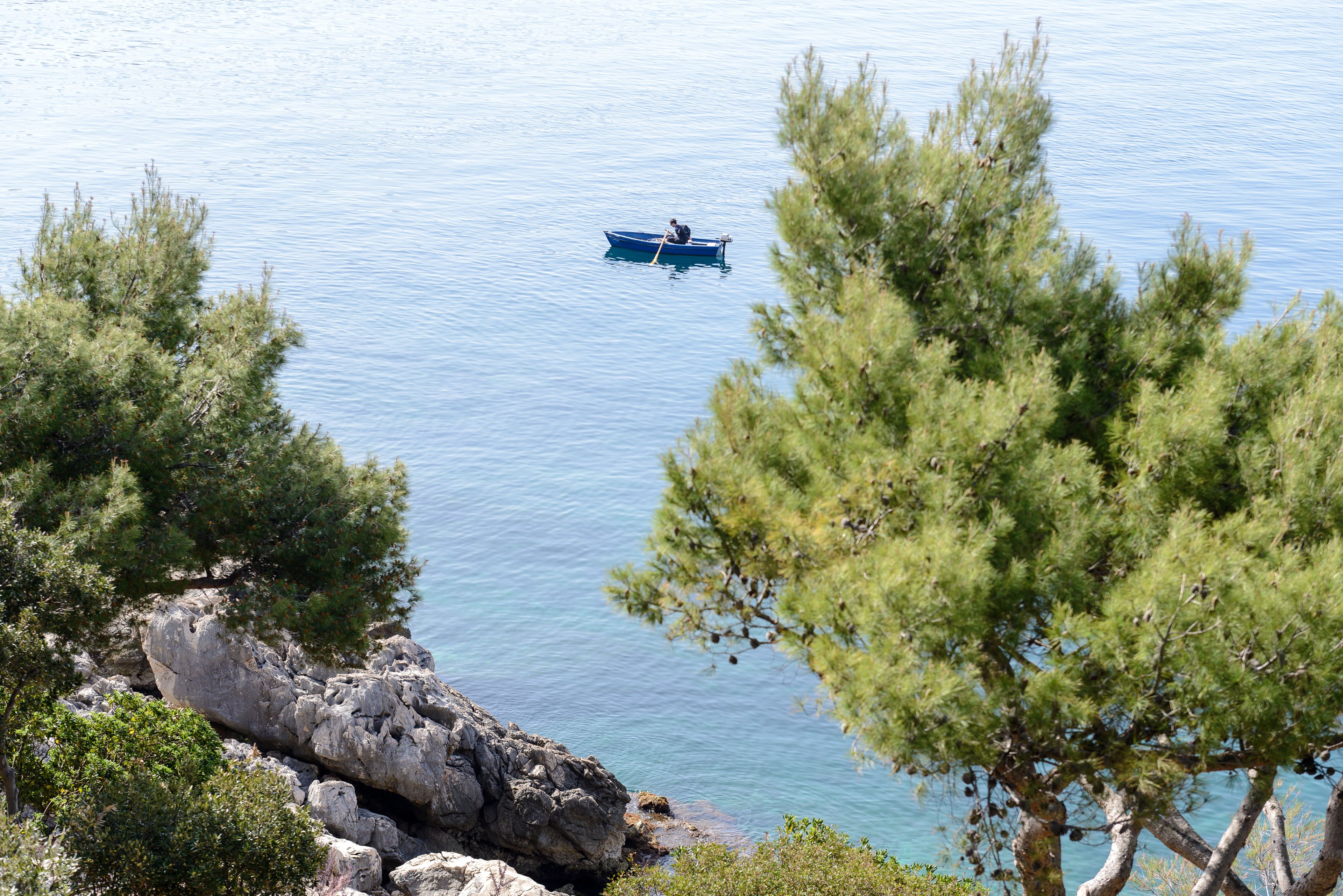 A calm lake with a small boat anchored near the shore, surrounded by pine trees and rocky terrain.