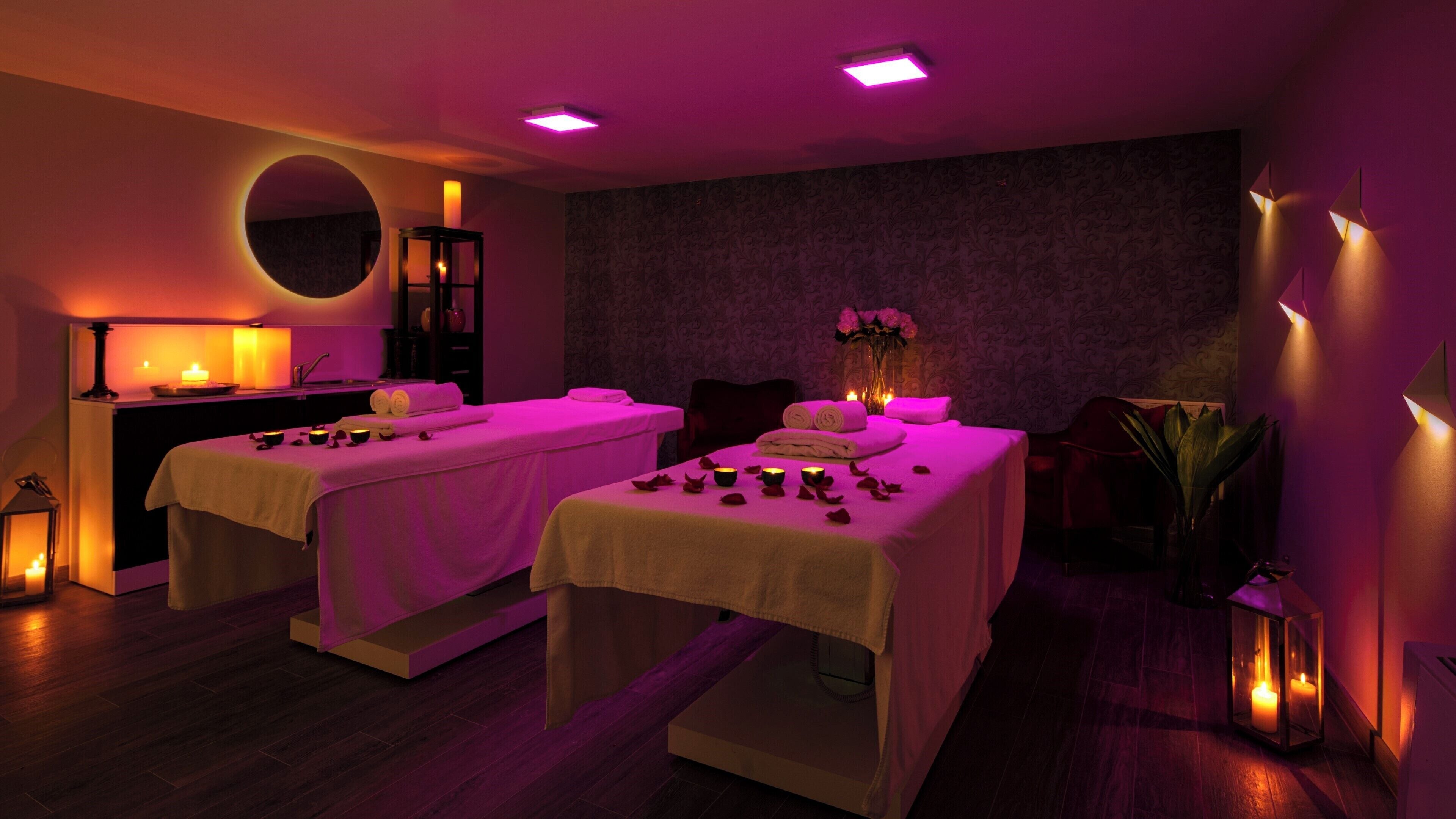 A spa room with two massage tables, candles, and a mirror.