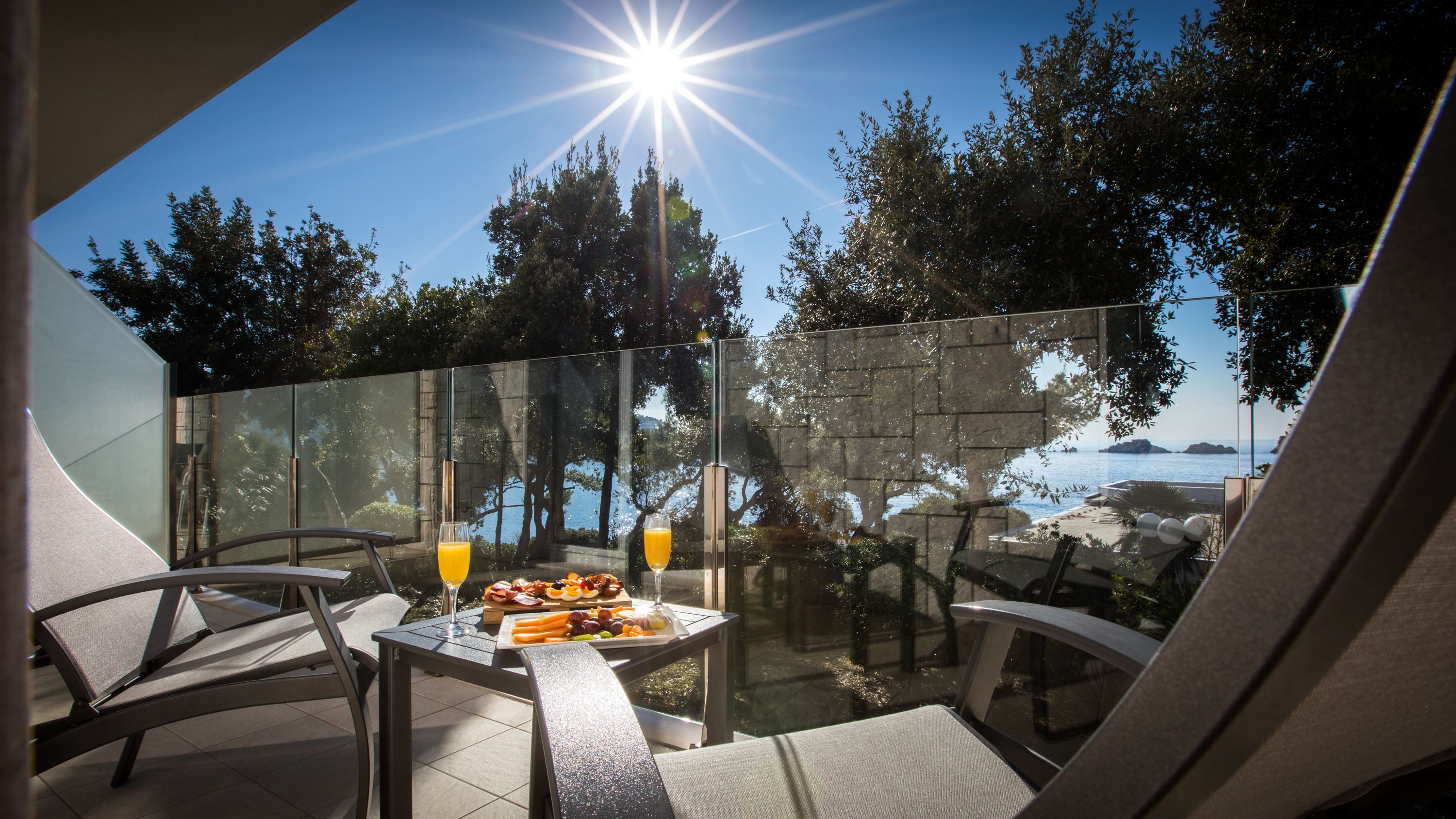 An outdoor dining area with a table set for two, featuring a glass of orange juice and a fruit platter.