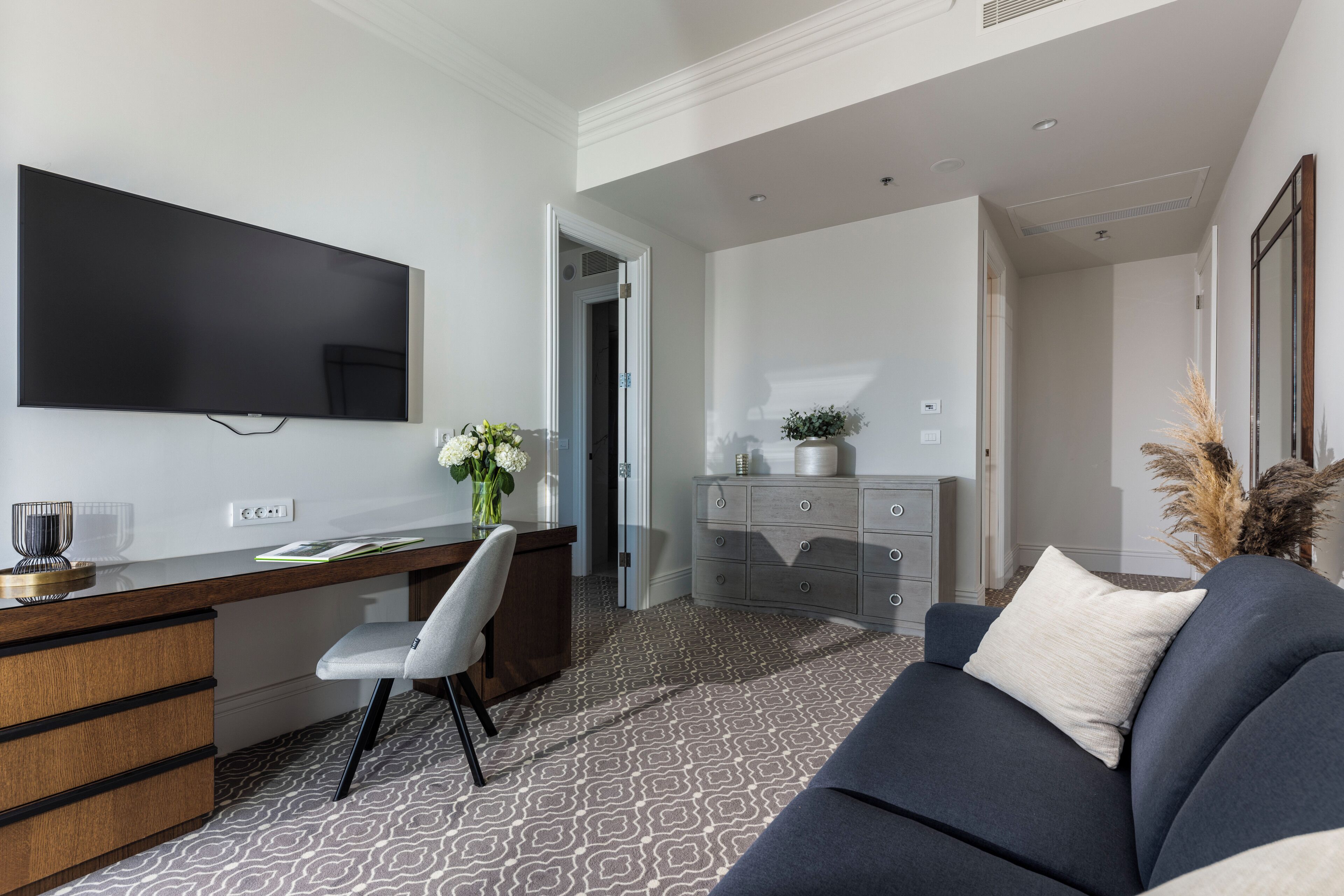 Una sala de estar moderna con un televisor de pantalla plana, un escritorio con una silla, un sofá y un jarrón decorativo.