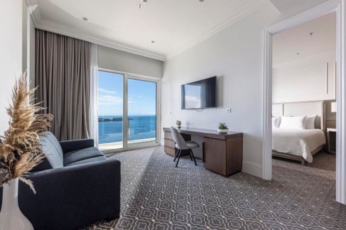 Habitación de hotel con un ventanal grande, un escritorio, una cama y un televisor.