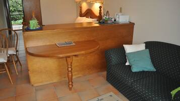 Una habitación con un mostrador de recepción de madera, un sofá con un cojín verde azulado, una silla y una alfombra pequeña.