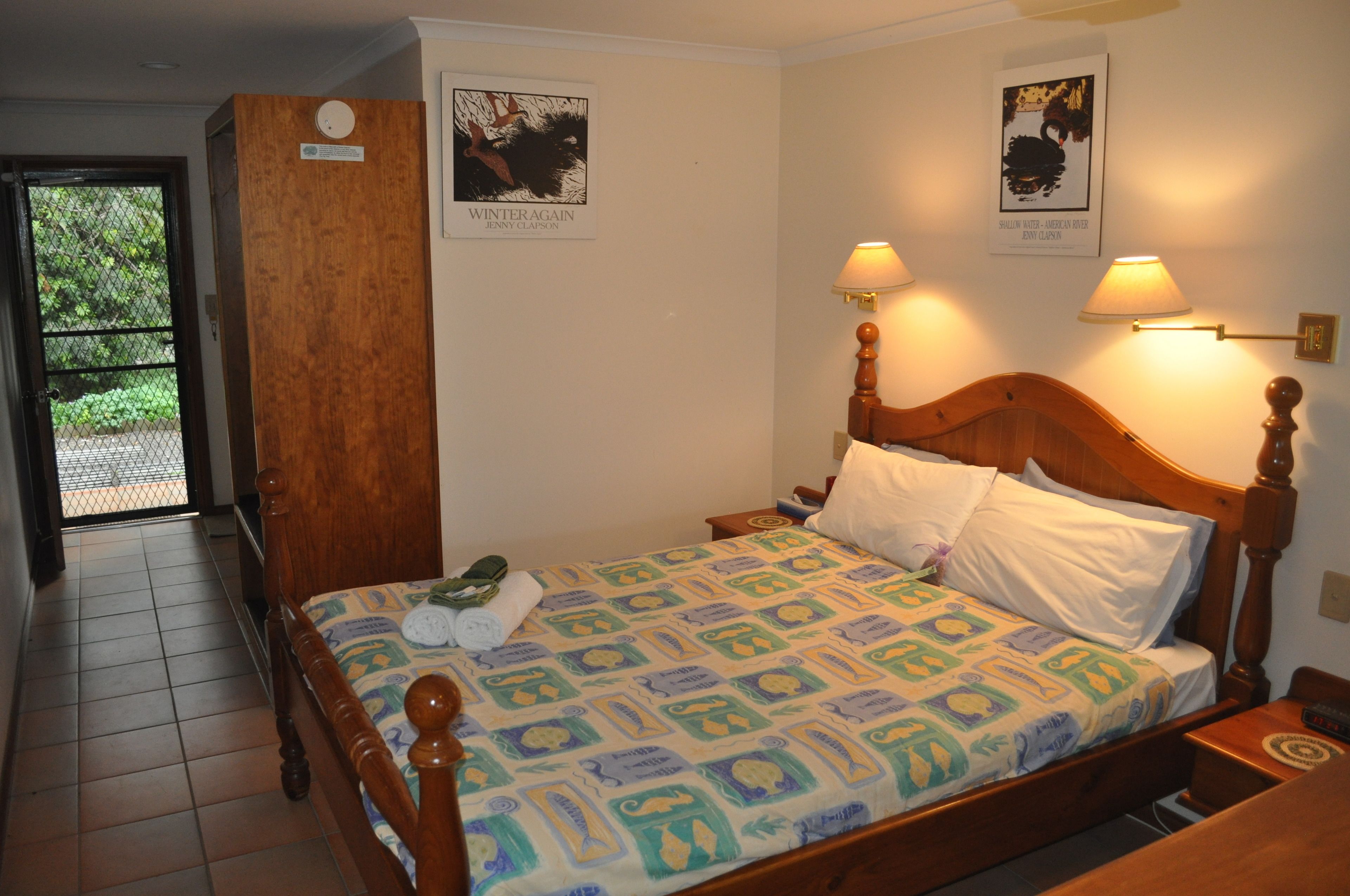 Una habitación de hotel con una cama de madera, dos lámparas fijadas a la pared y dos carteles enmarcados.