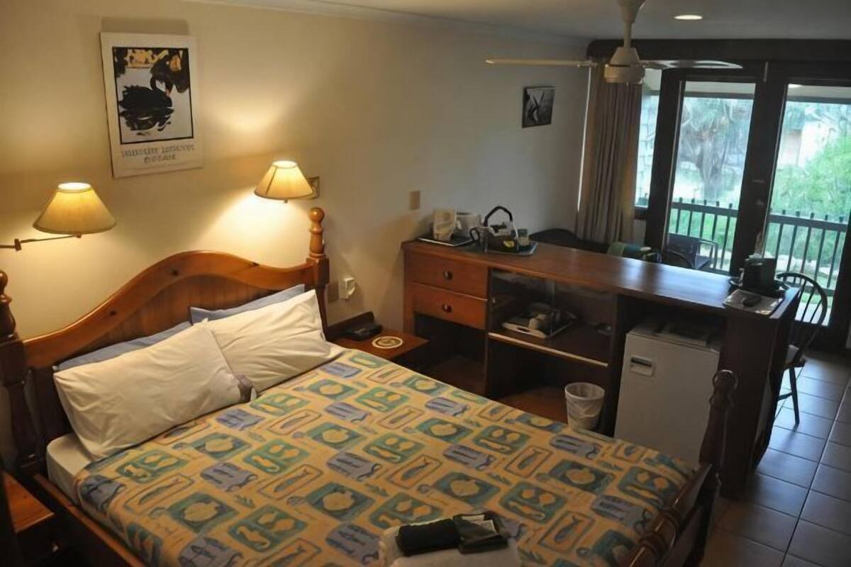 Une chambre d’hôtel comprenant un lit, des lampes de chevet, un bureau avec une chaise, un petit réfrigérateur et un balcon avec vue.
