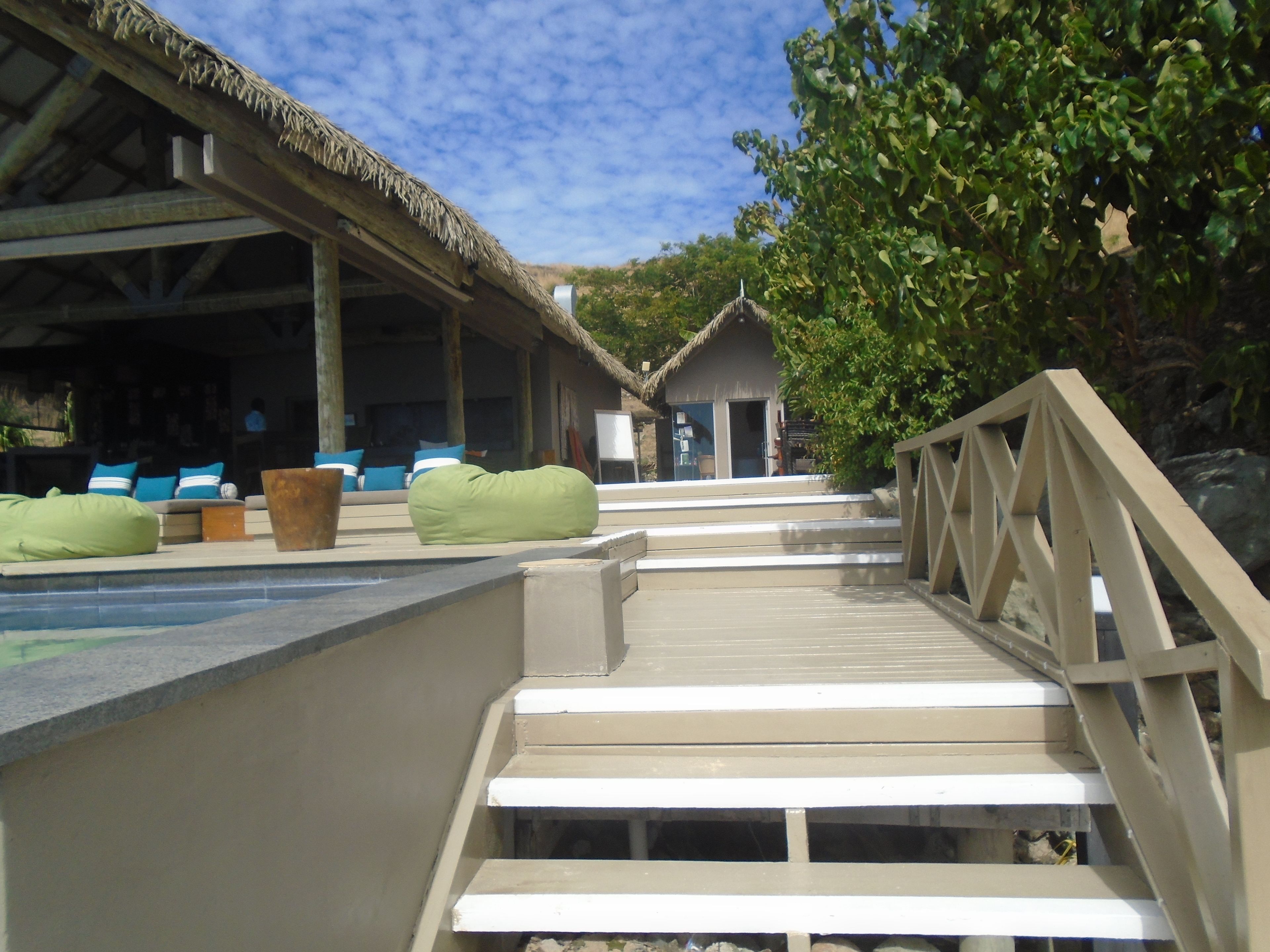 A wooden staircase leading to a thatched-roof building with outdoor seating.