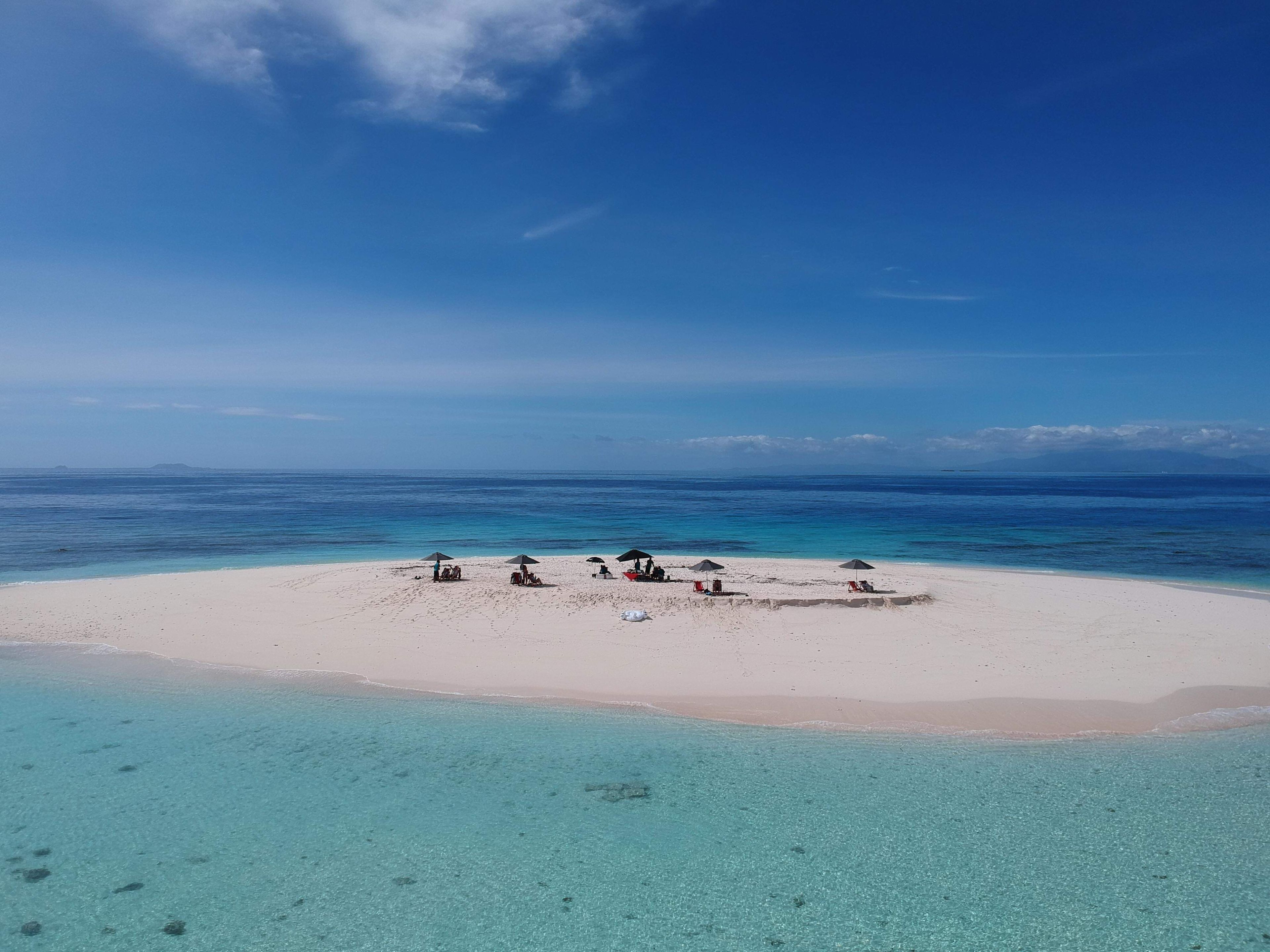 Una playa con agua turquesa cristalina y una orilla de arena. Varias sombrillas y sillas de playa están dispuestas para tomar el sol.