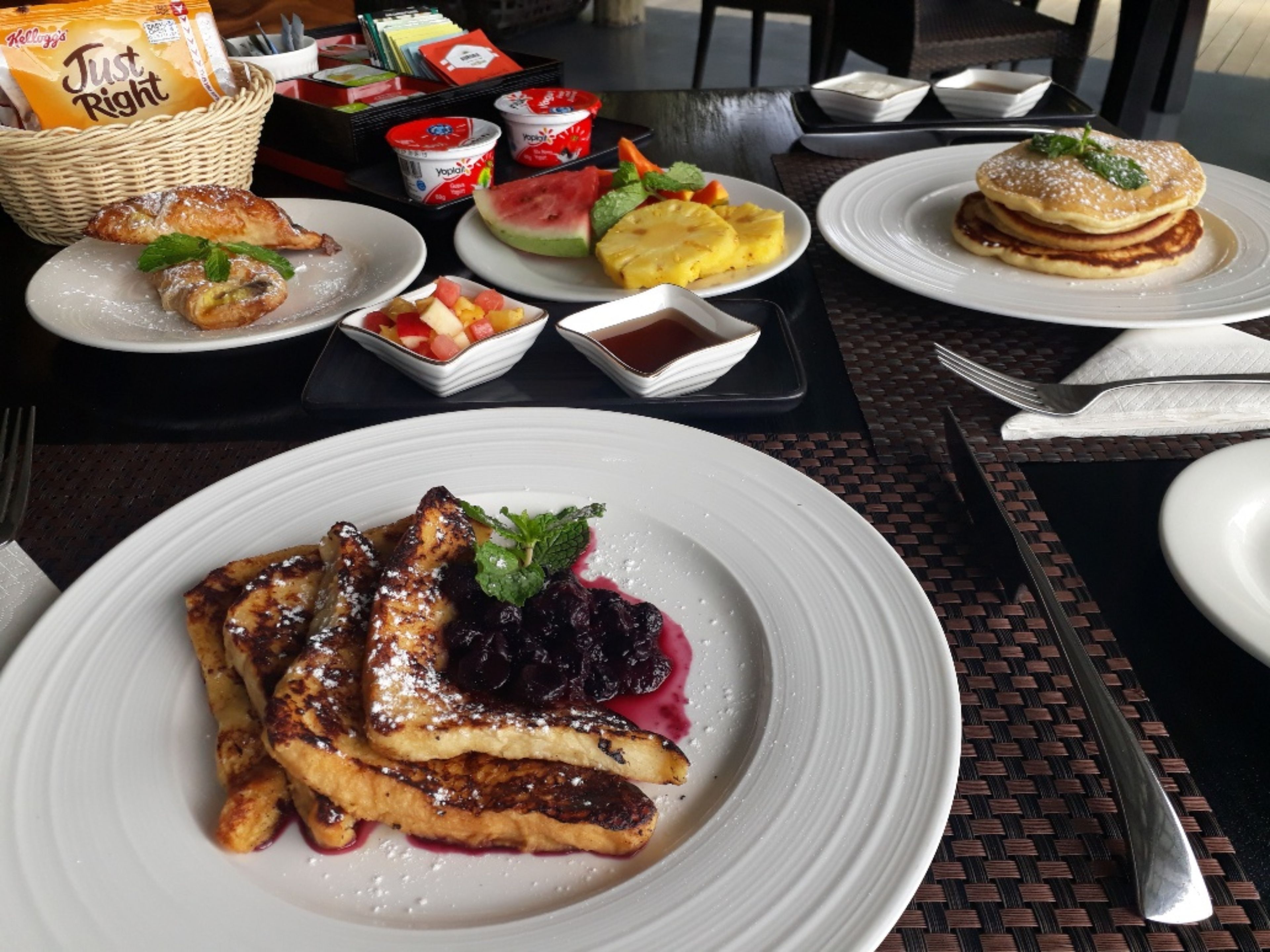 A breakfast setting with pancakes, waffles, and fruit on white plates.