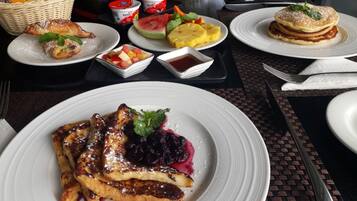 A breakfast setting with pancakes, waffles, and fruit on white plates.