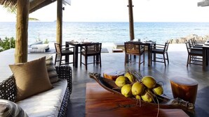 An outdoor seating area with a view of the ocean, featuring wooden furniture and a bowl of coconuts. - Tadrai Island Resort-Fiji - All Inclusive (Mana Island)