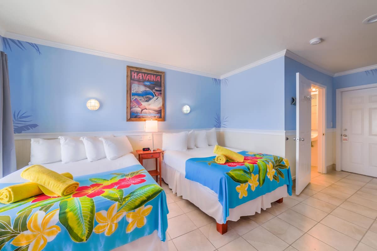 A hotel room with two beds, each with a floral bedspread, a nightstand, a wall-mounted lamp, and a poster of Havana.