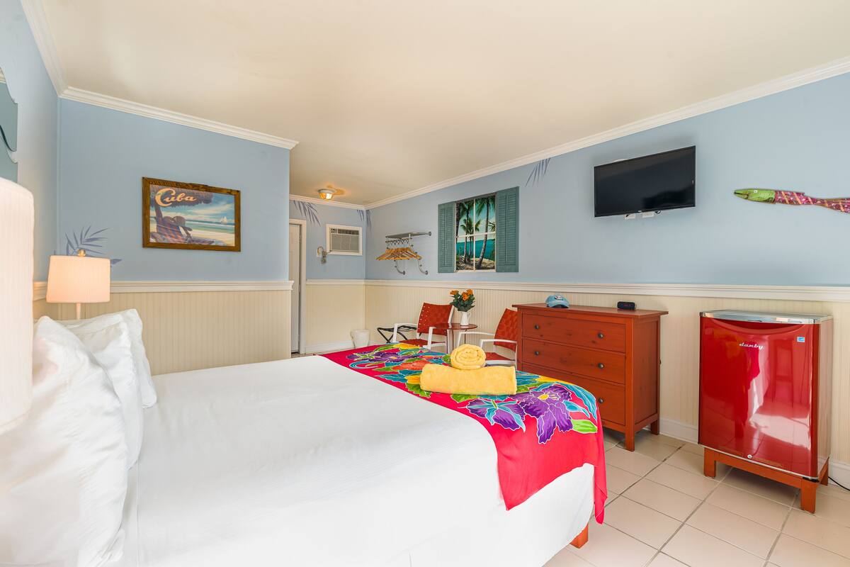 A hotel room with a bed, a dresser, a television, and a small refrigerator.