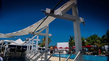 A poolside area with a white canopy, palm trees, and a clear blue sky.