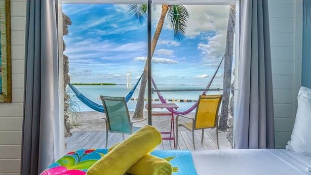 Una camera d'albergo con un letto, vista sulla spiaggia, un'amaca e sedie da spiaggia.