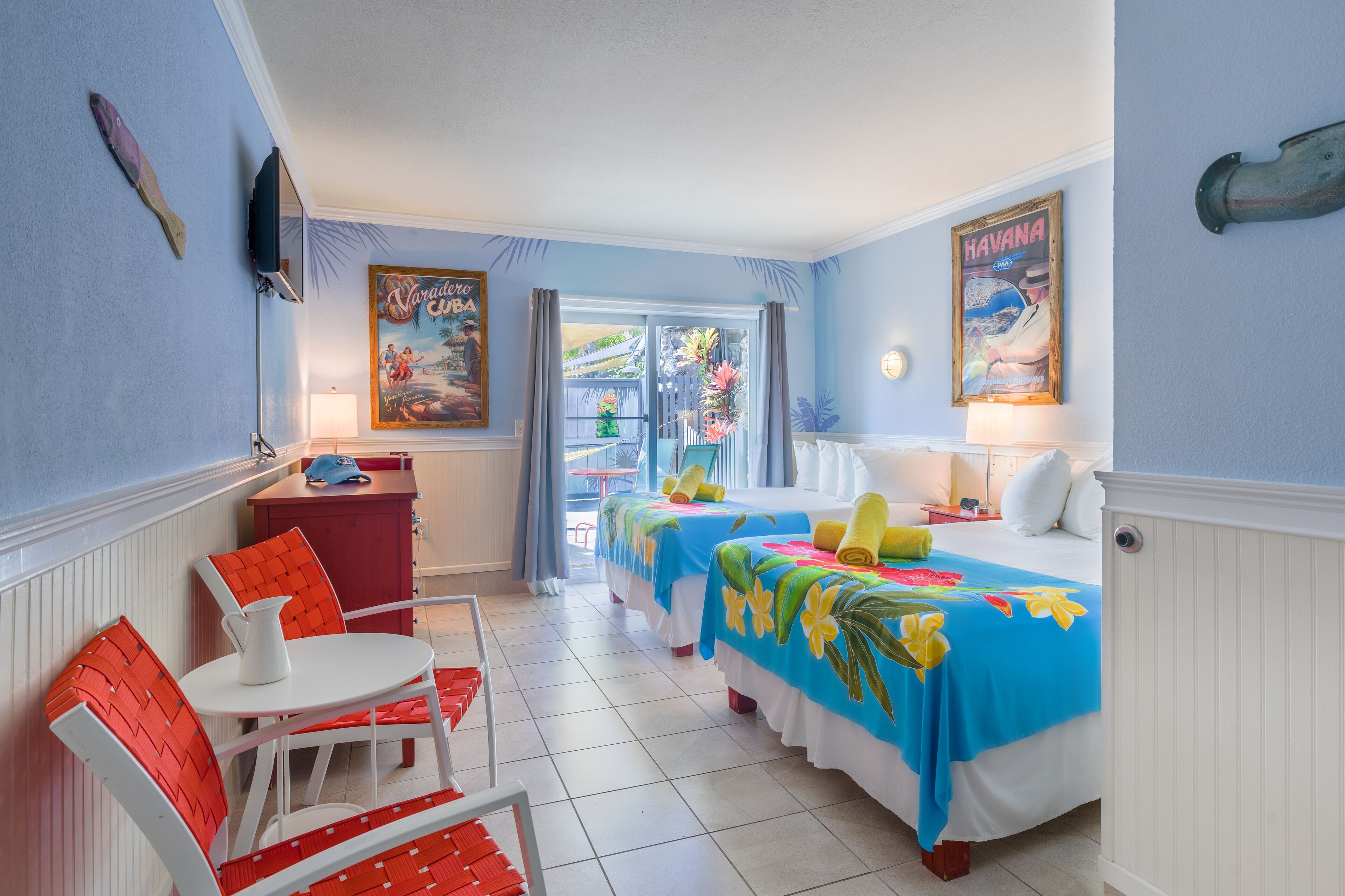 A hotel room with two beds, a small table, chairs, a TV, and a balcony with a view.