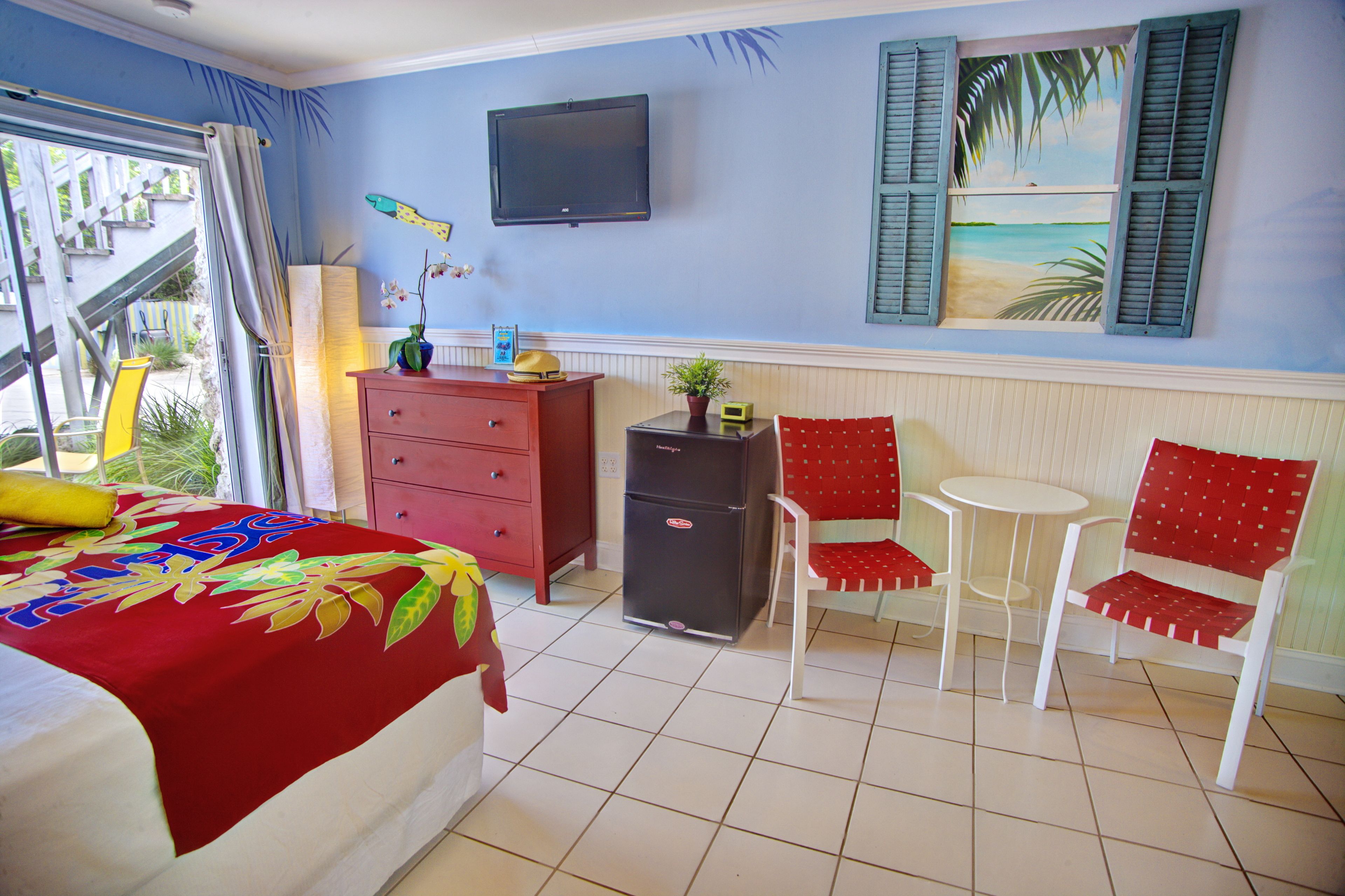 A room with a bed, a dresser, a TV, two chairs, and a small table.