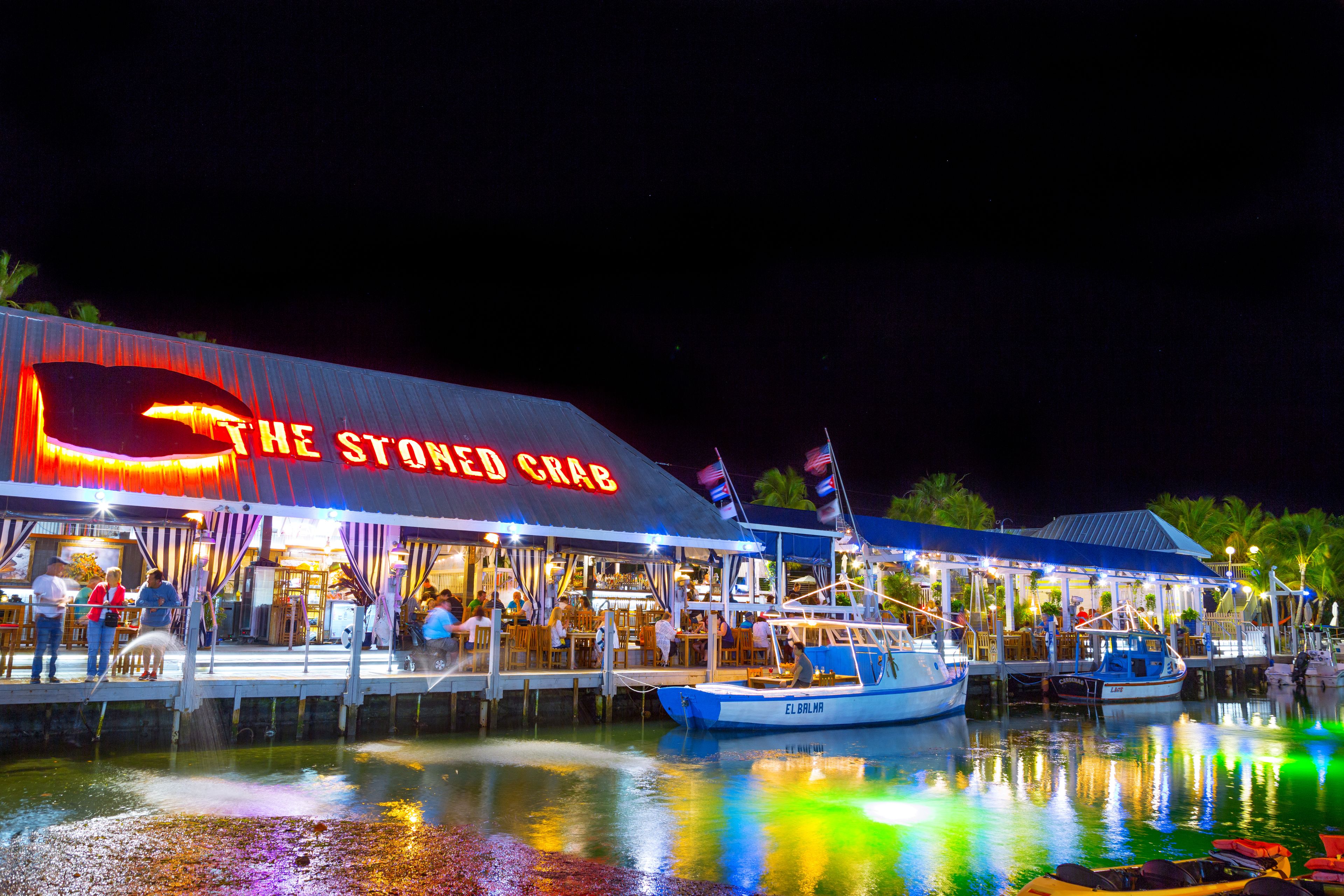 Un restaurante frente al agua llamado "The Stoned Crab" con terraza y barcos amarrados cerca.