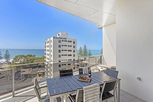 Un balcón con mesa lista para comer, con vistas a la ciudad y al mar.