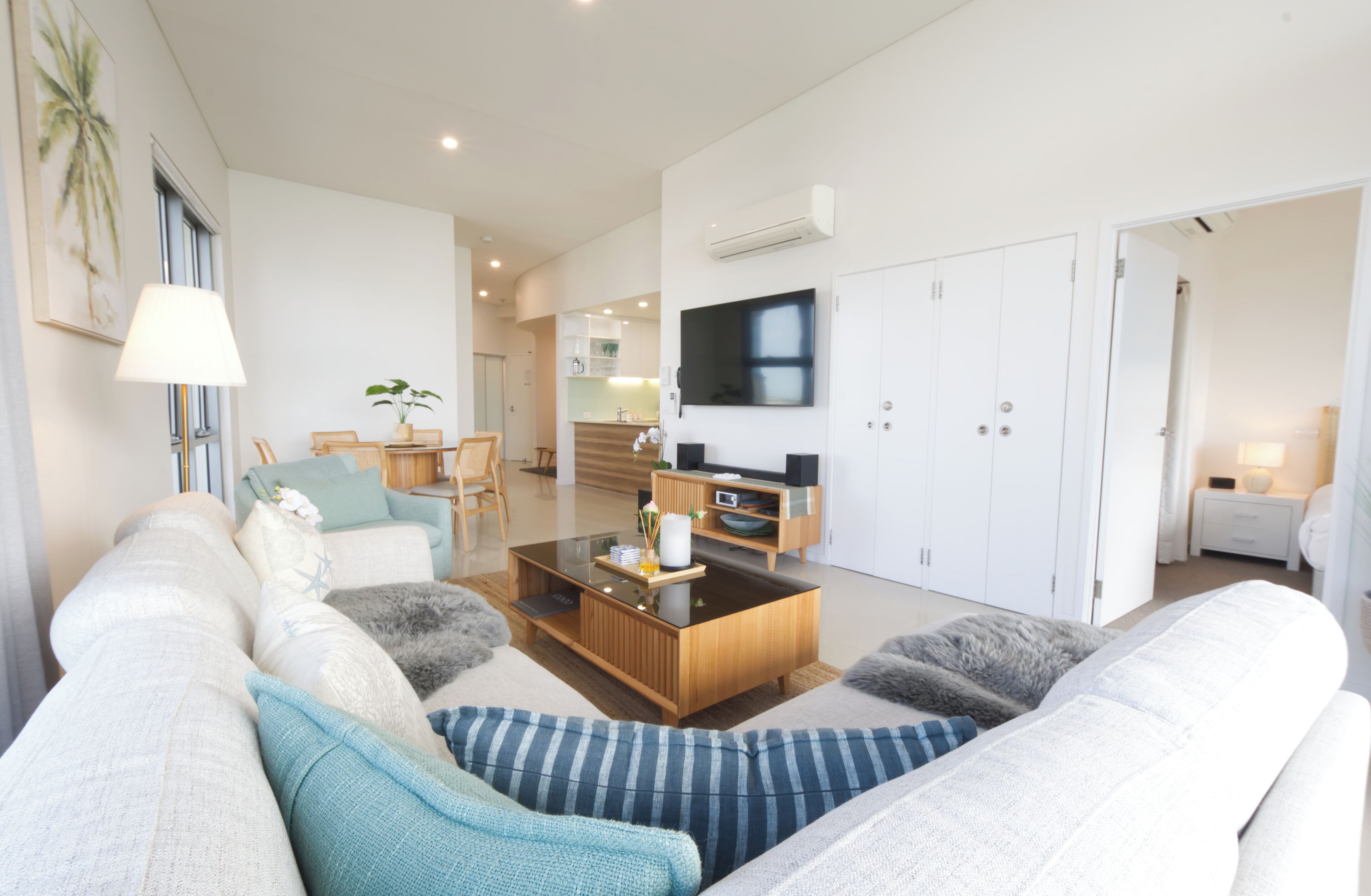 A modern living room with a sofa, coffee table, and TV. There is a kitchen in the background.