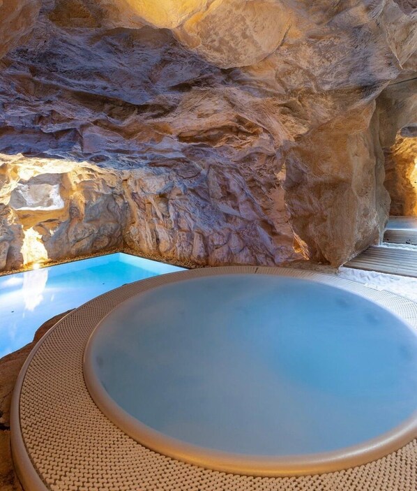 A hot tub with a clear blue pool, set against a rocky backdrop.