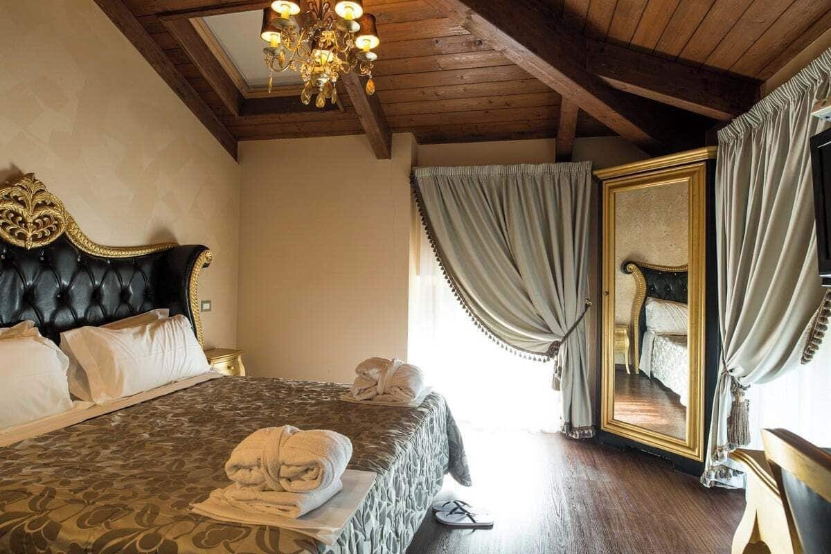 Ein Hotelzimmer mit einem großen Bett, einer Chandelier, einem Spiegel und Vorhängen.