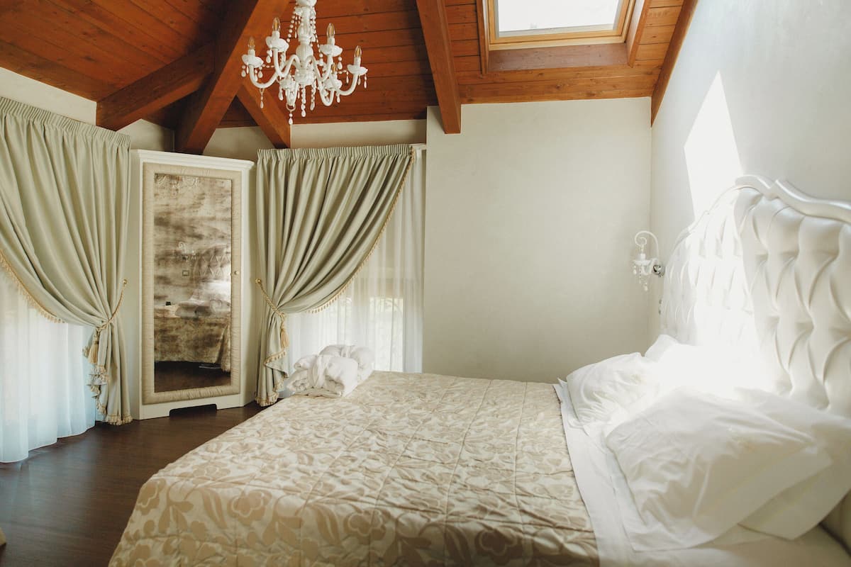 Ein Schlafzimmer mit einem großen Bett, Holzbalkendecke, einer Chandelier und einem fenster mit Vorhängen.