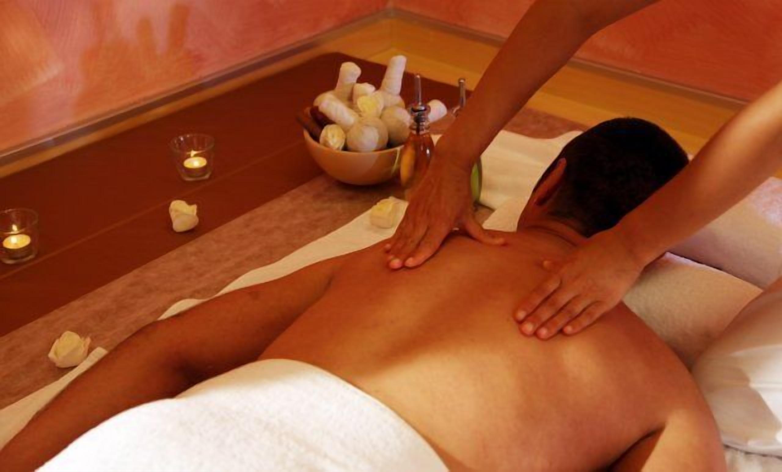 Een persoon ontvangt een rugmassage in een spa, met kaarsen en een schaal stenen.