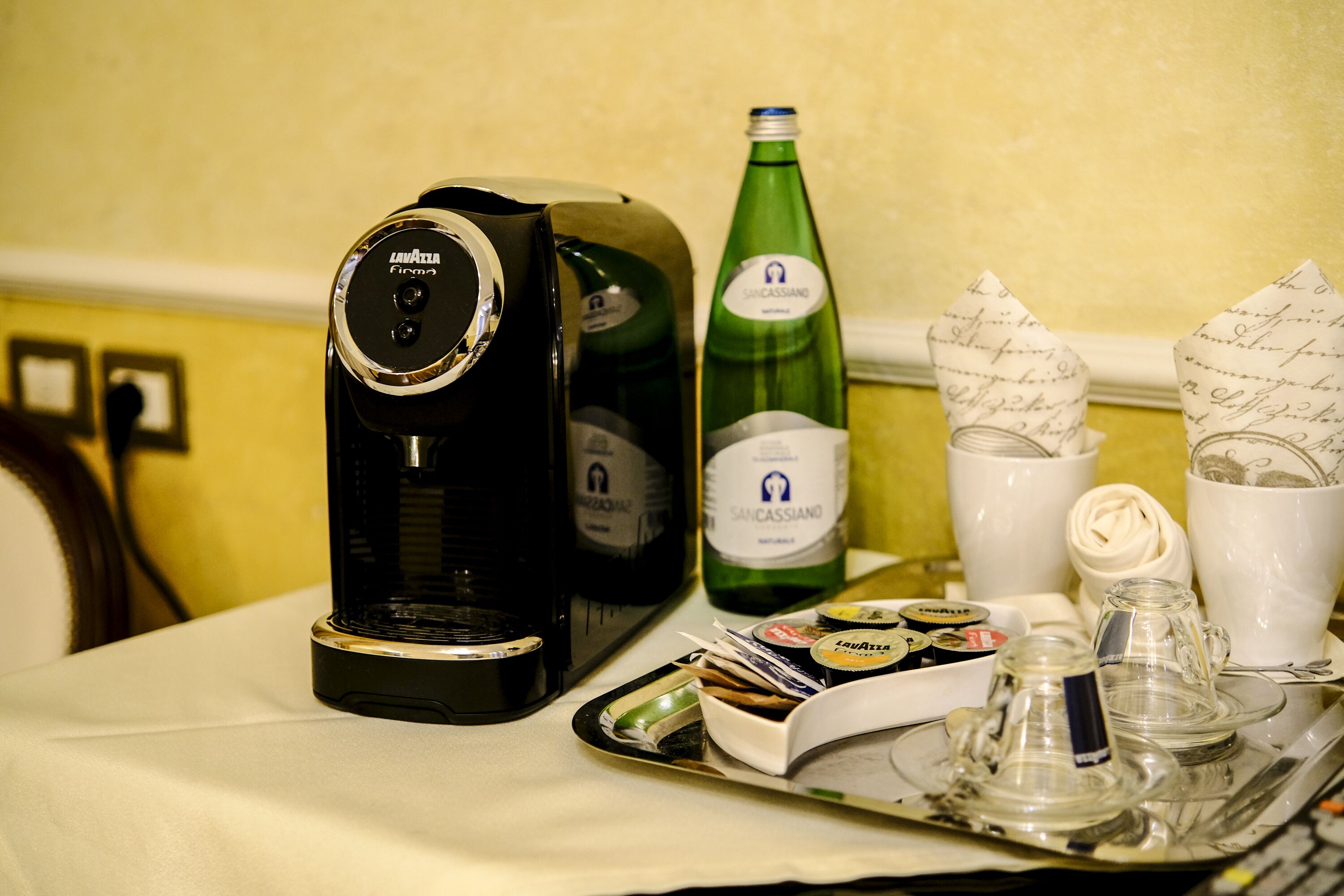 A coffee maker, a bottle of wine, and a tray with condiments and utensils on a table.