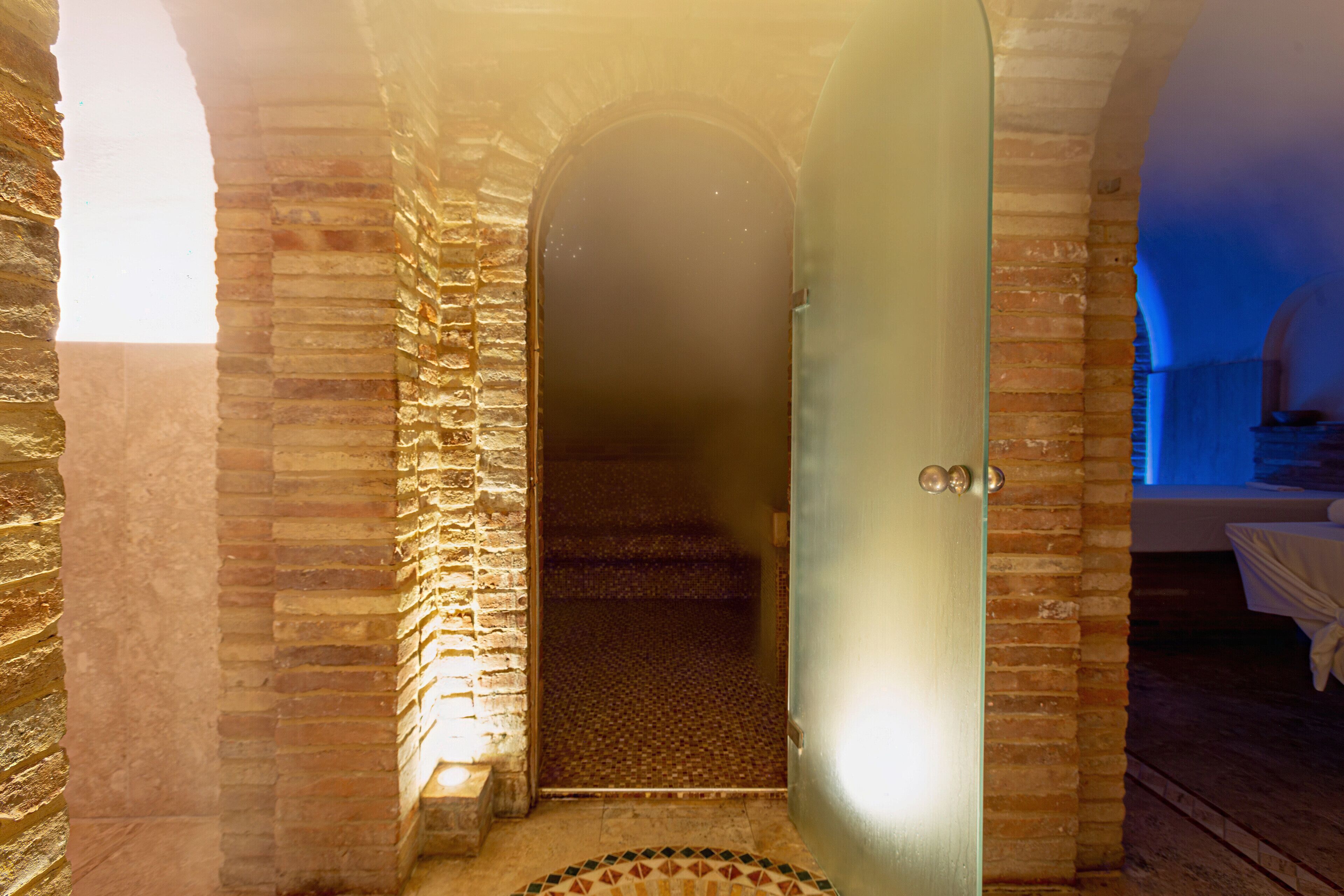 A stone-walled hallway leading to a room with a tiled floor and a door with a glass panel.
