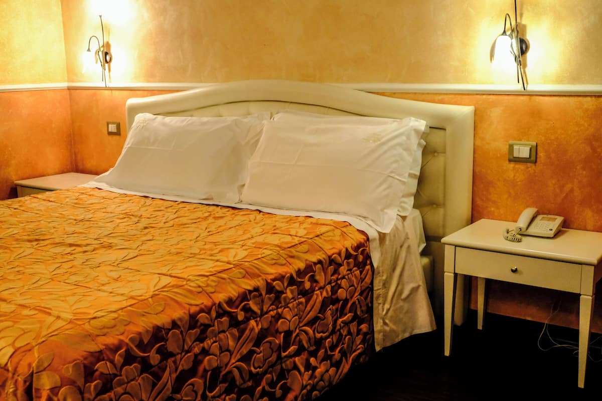 Ein Hotelzimmer mit einem Bett, einem Nachttisch mit Telefon und Wandleuchten.