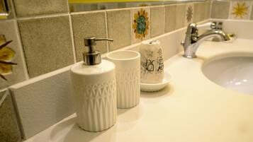 A bathroom sink with a white countertop, a silver faucet, and two white ceramic cups with a pump dispenser.
