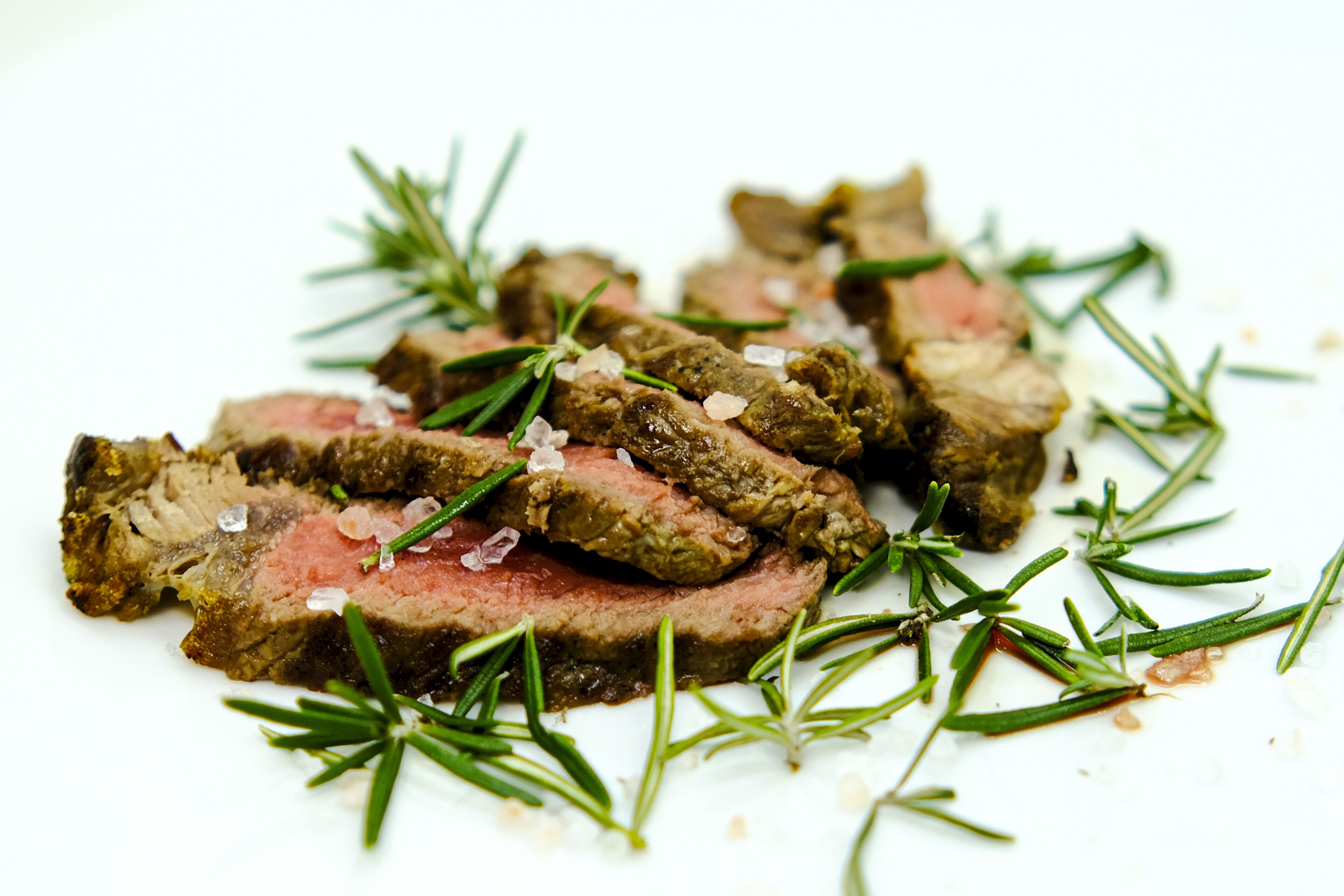 A plate of sliced meat with rosemary and coarse salt.