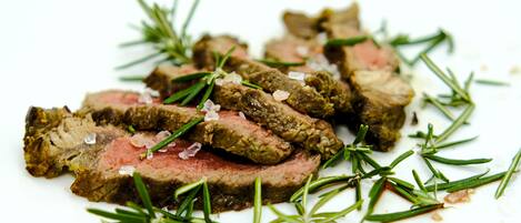 A plate of sliced meat with rosemary and coarse salt.