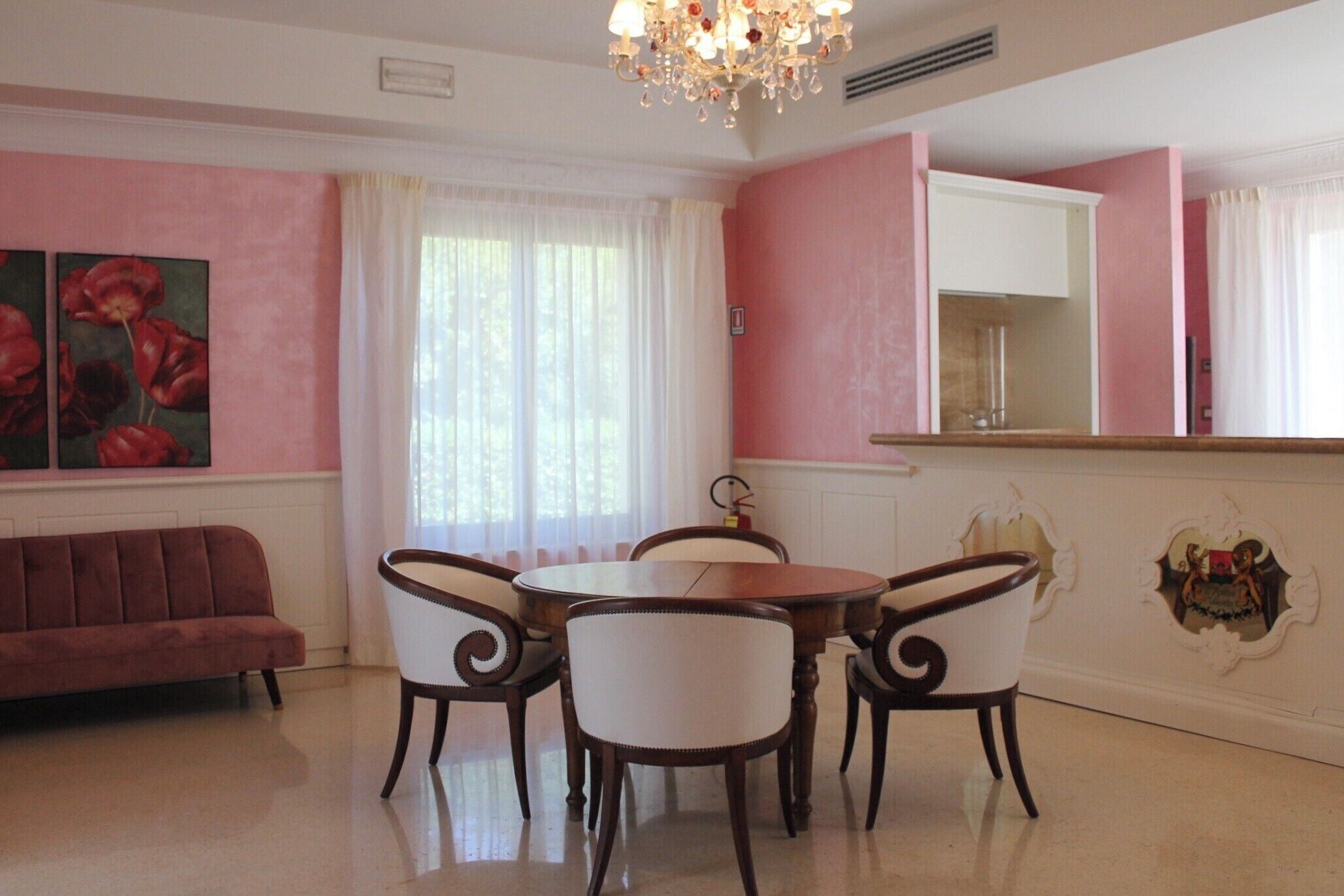 A dining area with a round table, four chairs, a sofa, and a chandelier.