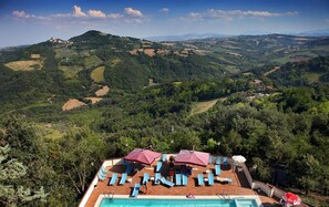 Zona junto a la piscina con sillas de descanso y sombrillas, con vistas a un paisaje montañoso.